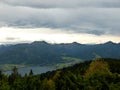 Imposing landscape with trees behind it a lake and mountains in the background with clouds