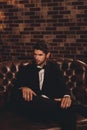 Imposing young man in elegant black suit sitting on couch