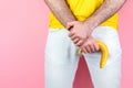 Impotence and men`s health. A man in white jeans, legs apart, holds a limp banana near the genitals. Pink background. Close up.