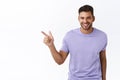 Impressed handsome bearded hispanic man in purple t-shirt, pointing left and smiling amused, sharing information where Royalty Free Stock Photo