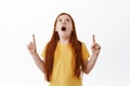 Impressed redhead little girl with freckles, drop jaw and gasping, pointing and looking up at something awesome. Shocked Royalty Free Stock Photo