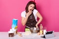 Impressed surprised emotional model poses isolated over pink background, wearing brown apron and white t shirt , talking over her