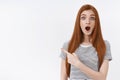 Impressed surprised emotive redhead young girl drop jaw say wow widen eyes astonished pointing upper left corner amazed