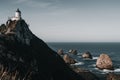 impressive lighthouse built on top of a large rock next to plants and the ocean under a clear sky, nugget point, new Royalty Free Stock Photo