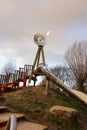 Impressive playground slide with a windmill on top . Heavy dark clouds and blank trees in the background of the playground . Empty Royalty Free Stock Photo