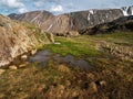 Impressive scenery with puddles on a stony meadow and vast mountains in sunlight. Wet mountain meadow