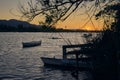 Impressive sunset on the lake from the jetty with some boats floating and a tree in the foreground framing the picture