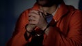 Imprisoned male in handcuffs holding cross and praying, feeling guilty, regret