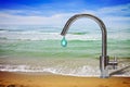 An improbable faucet at the seaside is pouring a drop of water