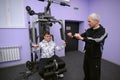 Improving motor control. Man therapist teaching disabled boy of training on the exersice machine. Municipal Department