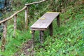 Improvised homemade bench made from wooden board supported with cut wooden sticks next to small fence at local river bank Royalty Free Stock Photo