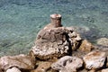 Improvised homemade stone mooring bollard with rusted metal hook on top built on top of large rock formation