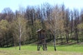 Improvised old hunting lookout tower made of wood surrounded with grass and tall trees with clear blue sky in background