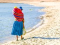 Incan woman with baby in the colorful scarf on a back. Walks on the beach of Island of the Sun at Titicaca Lake, Bolivia