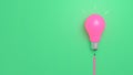 Incandescent light bulb with pink bulb and pencil-shaped switch string on a background of green paper