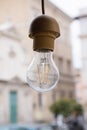 Incandescent transparent lamp without shade hanging on a wire outdoors. Blurred Roman antic church in background