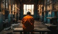 Incarcerated person in orange jumpsuit sitting alone in a bleak prison cell, gazing out of the barred window, evoking themes Royalty Free Stock Photo