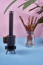 Incense burner on a blue table with a pink background and a glass with colored incense and a green plant.