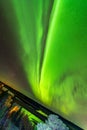 Inclined earth and bright green aurora lights almost on the whole sky over tree tops in Sweden, river, city lights and lake, clear Royalty Free Stock Photo