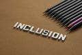 Inclusion word, black pencils and one pink pencil over brown background. Equality, acceptance, right concept. Top view. Royalty Free Stock Photo