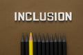 Inclusion word with black pencils and one yellow pencil over brown background. Equality, community integration concept. Top view