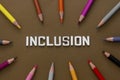Inclusion word with colorful pencils over brown background. Equality, community integration concept. Top view