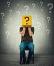 Incognito young man seated on a chair holding a yellow box with question mark instead of head Royalty Free Stock Photo
