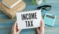 Income Tax text on paper sheet with magnifying glass on chart, dice, spectacles, pen, laptop and blue and yellow push pin on Royalty Free Stock Photo