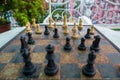 Incomplete set of chess pieces arranged on a rusted chess board with a bench in the background