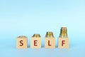 Increasing stack of coins with word self on wooden blocks in blue background. Invest on yourself improvement.