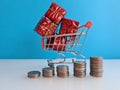 Increasing stacks of coins and basket with gift on blue background