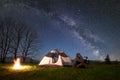 Man with photo camera sitting alone near tourist tent at campfire under dark blue starry sky Royalty Free Stock Photo