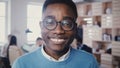 Incredible close-up portrait of handsome young African American man in glasses smiling at camera in busy office 4K. Royalty Free Stock Photo