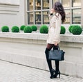 Incredible Long-legged brunette girl with long hair, dressed in a raincoat, high black boots with heels with a handbag