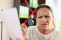 Incredulous middle age woman looking on document trough magnifying glass close-up.