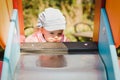 Indecision blond hair toddler girl in funny hat on a playground on a sliding in a public park