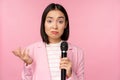 Indecisive, nervous asian business woman holding mic, shrugging and looking clueless, standing with microphone against