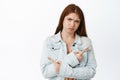 Indecisive redhead girl pointing sideways, choosing between two variants, troubled to make decision, standing over white