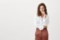 Independent attractive woman with successful look, standing in fashionable outfit, smiling while holding index finger on Royalty Free Stock Photo