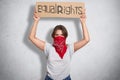 Independent confident young feminist standing over grey background in studio, raising her hands, holding sign equal