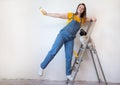 Happy woman makes repairs in her apartment. Funny female with a roller on ladder with copy space. Independent single Royalty Free Stock Photo