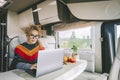 Independent woman sitting inside a camper van in smart remote working job activity using laptop. Concept digital nomad freedom