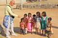 India, Hampi, 02 February 2018. A bald and cheerful European man gives gifts to Indian children. Joyful children are pulling their