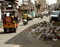 Rickshaws and motorcyclists ride down street full of garbage