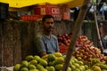 Indian adult male stands behind a vibrant display of a variety of fresh fruit on a table