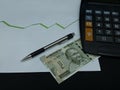 indian banknote, pen and calculator on background with rising trend green line