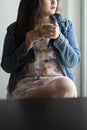 Indian Bengali beautiful and cute brunette girl in a casual blue jeans shirt and white top is drinking tea sitting on a chair Royalty Free Stock Photo