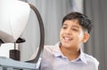 Indian boy doing eye test checking examination with autorefractor in optical shop, Optometrist doing sight testing for child