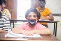 Indian boys students studying In classroom wearing mask maintaining social distancing looks at camera, school reopen during