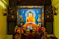 Indian Buddhist monk and people standing and praying on bare foot in front of large statue of lord Buddha inside Mahabodhi Temple.